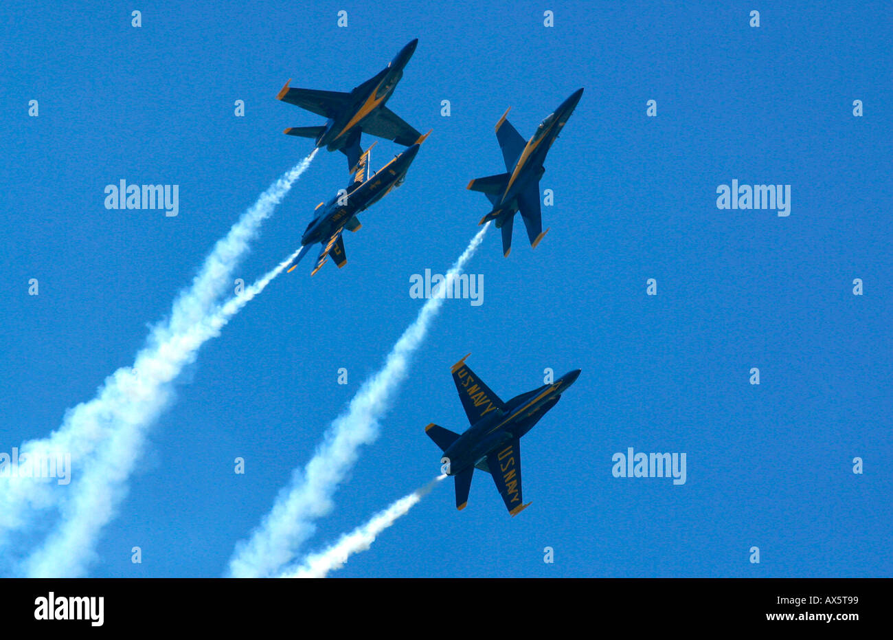 The Blue Angels FA 18s silhouetted breaking formation with trails of white smoke against a clear blue sky Stock Photo