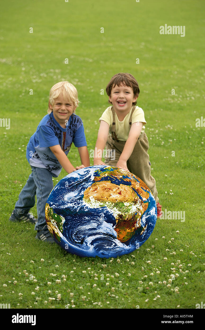 Children rolling a globe over a meadow Stock Photo