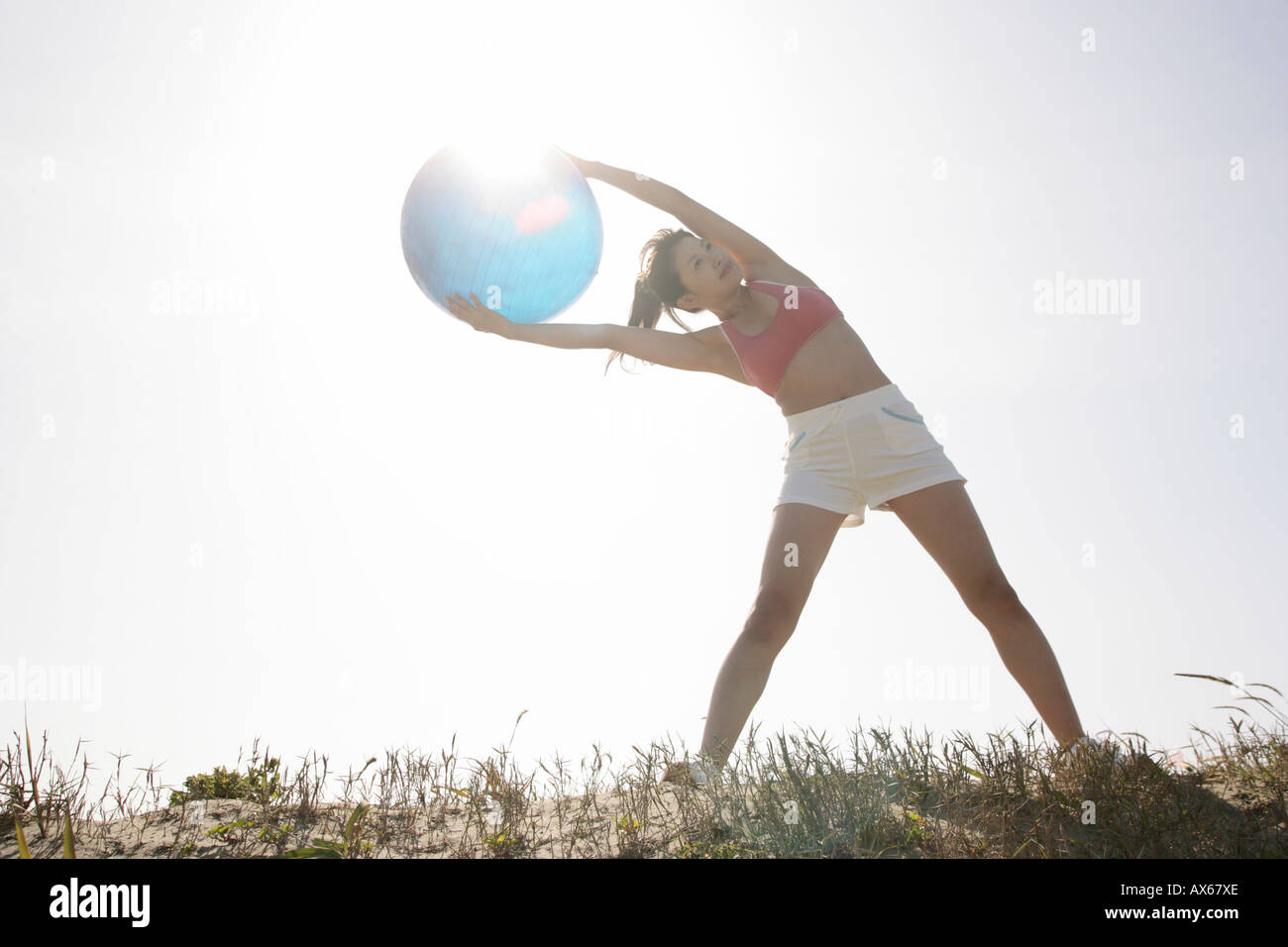 A young woman holds a huge ball as she bends from her abs while exercising under the sunlight Stock Photo