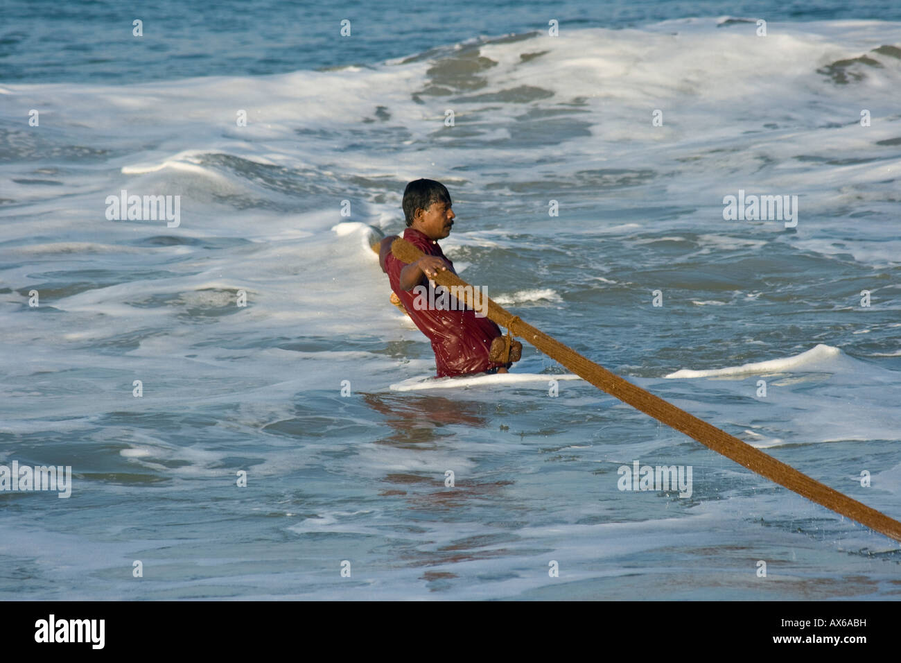 Man in the Ocean Pulling in Fishing nets on the Beach in Varkala India Stock Photo