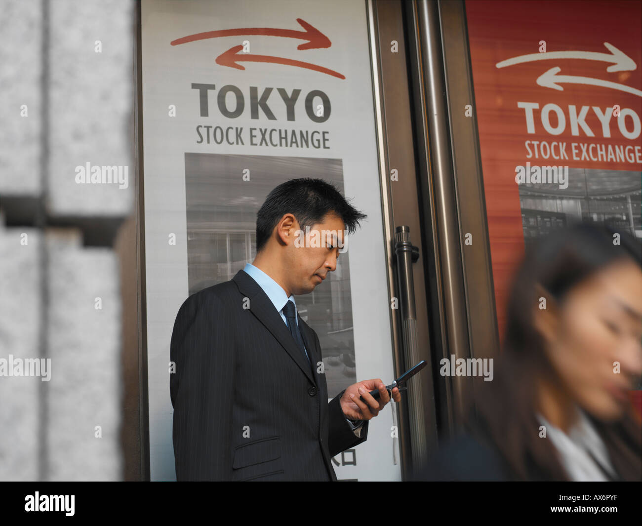A Japanese businessman with mobile phone outside the Tokyo stock exchange dials a number while other business people pass in fro Stock Photo