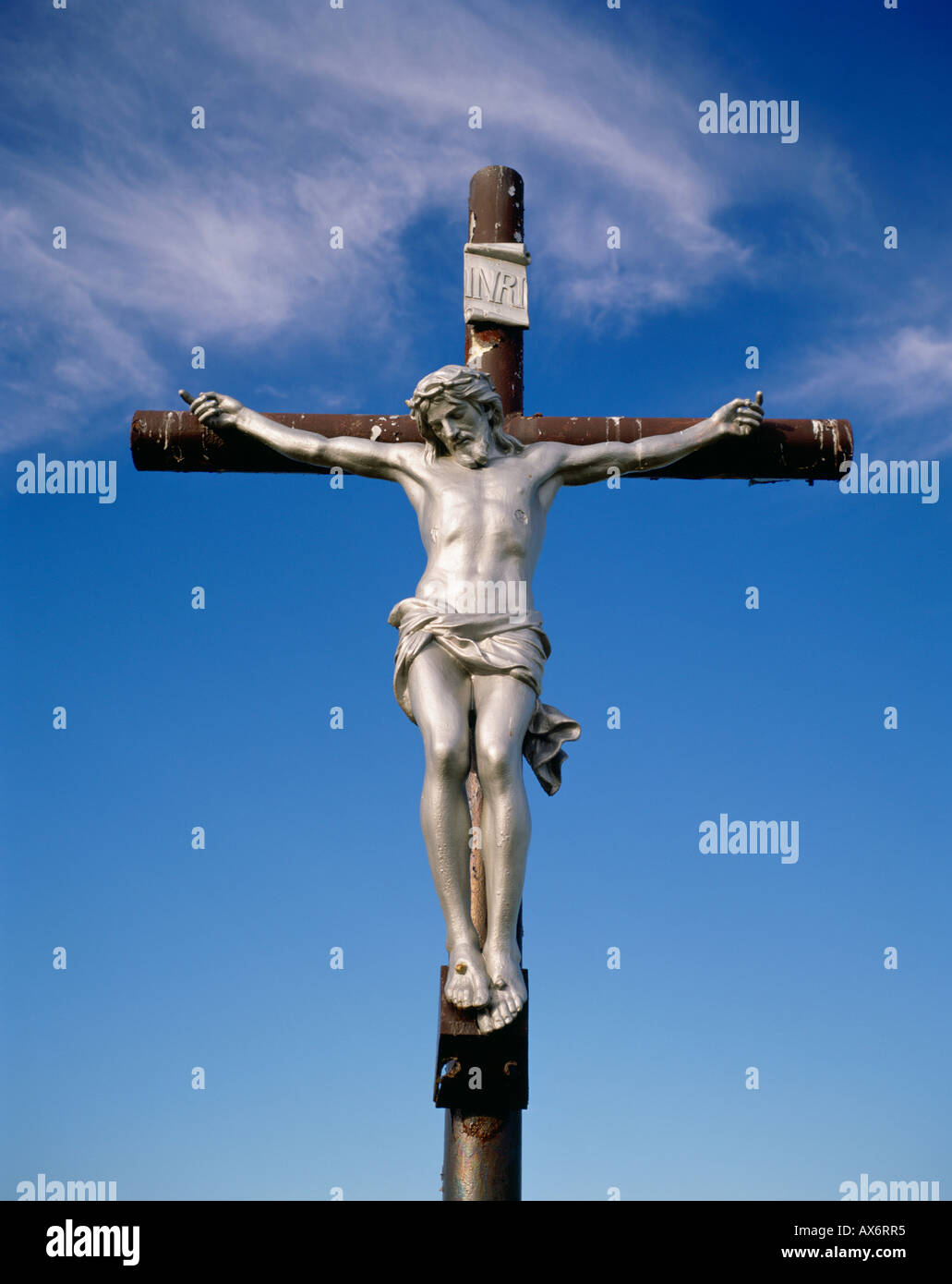 A silver colored Jesus Christ hangs on a crucifix in Nova Scotia Canada with a blue sky in the background Stock Photo