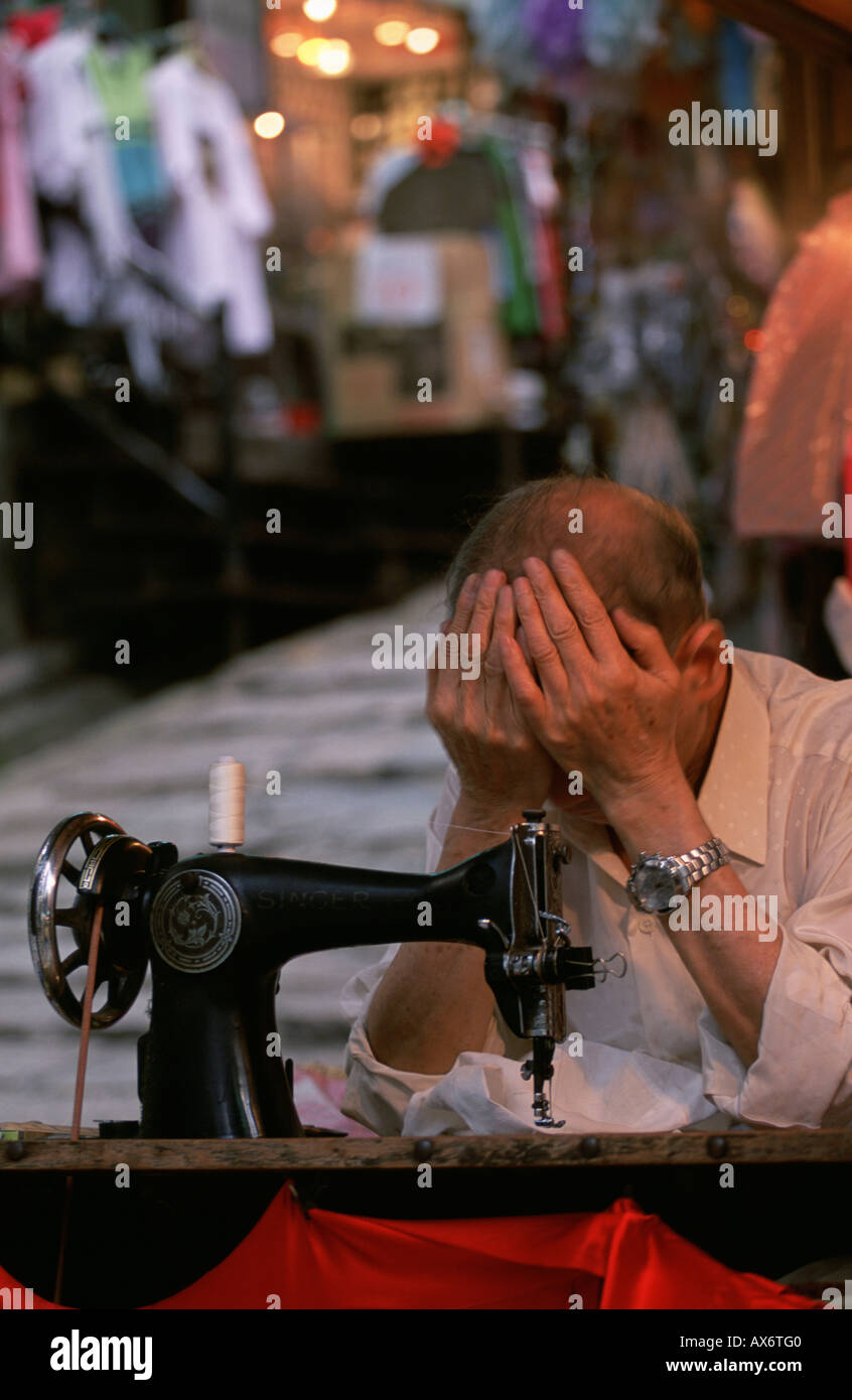 A tailor puts his head in his hands in front of his sewing machine