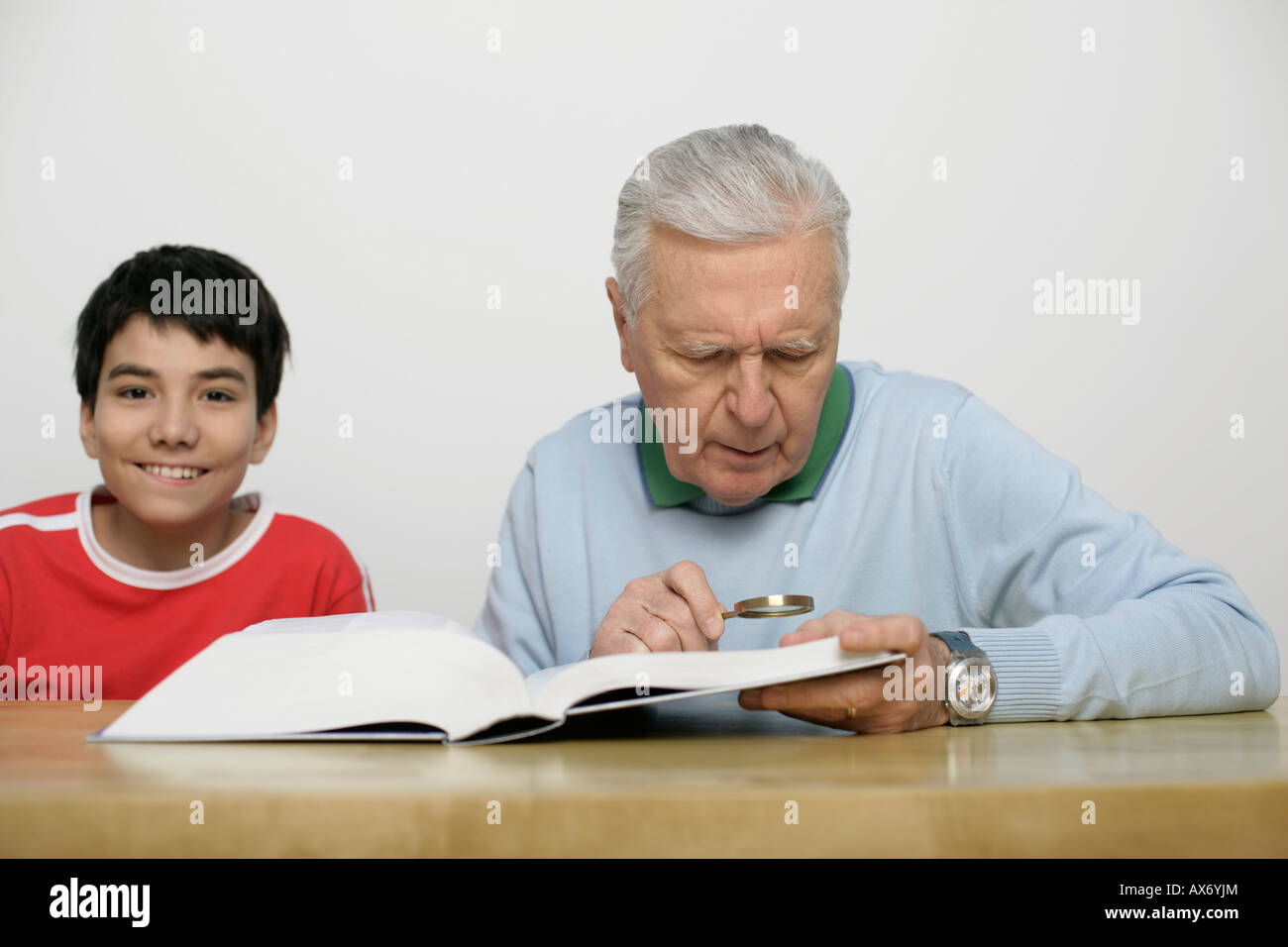 Grandfather using a magnifying glass to read a book, boy looking at camera, fully released Stock Photo