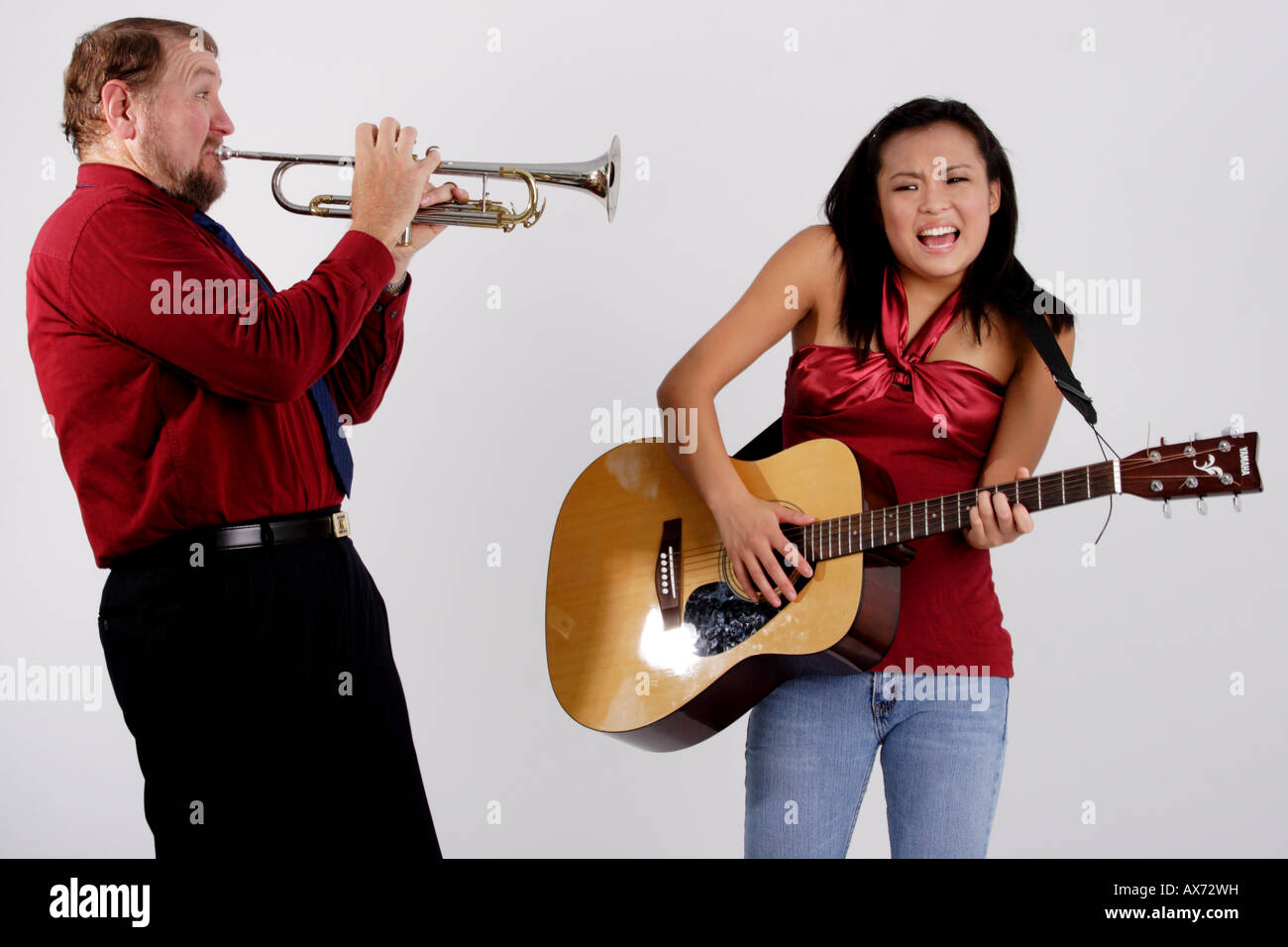 Stock Photograph of a man playing a trumpet into the ear of a teen girl with a guitar Stock Photo