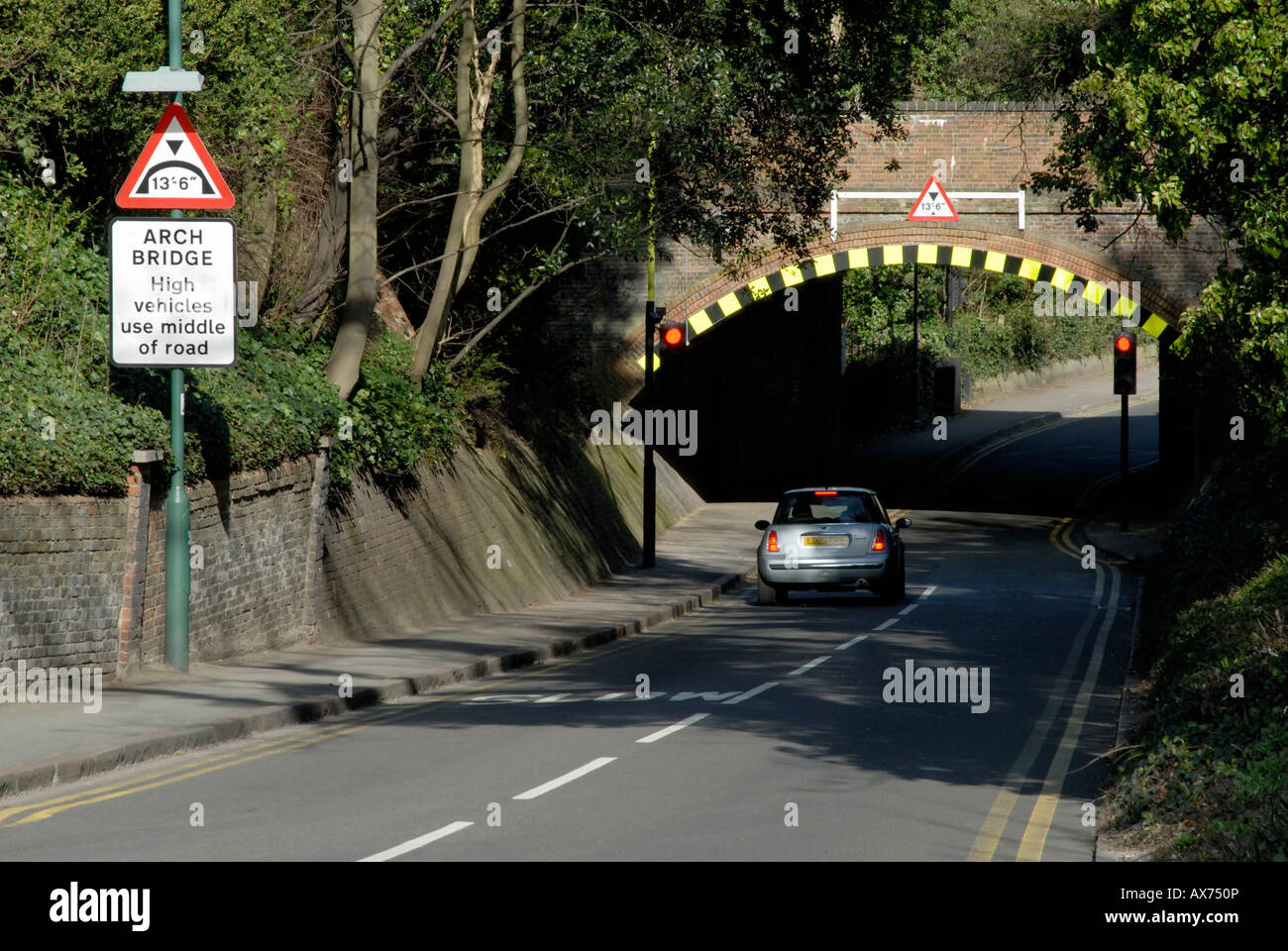 Low arch bridge with warning sign and high visibility markings and waiting car at red light, Cheam, south London, Surrey Stock Photo