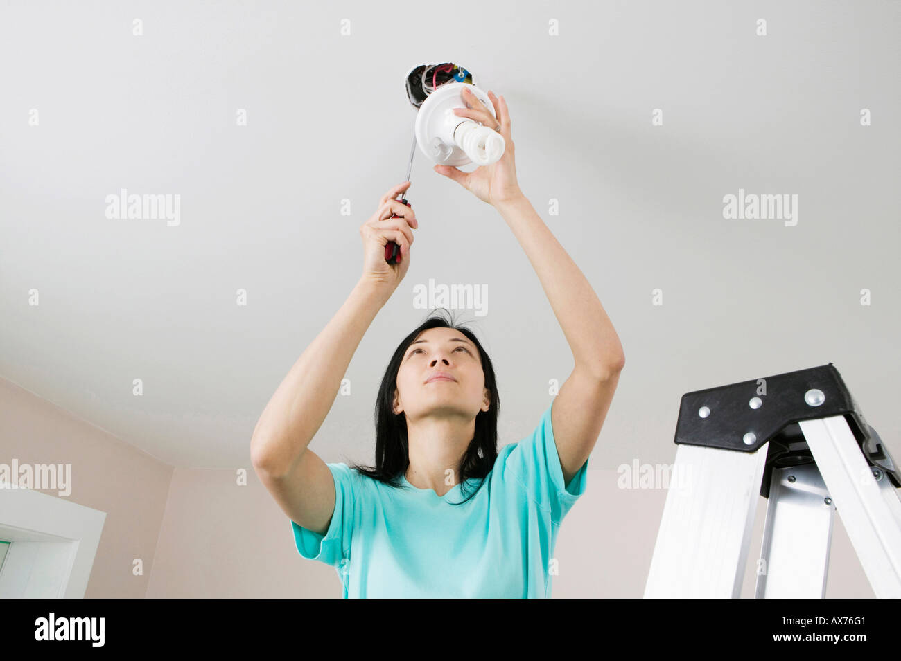 Low angle view of a young woman fixing a light fixture Stock Photo