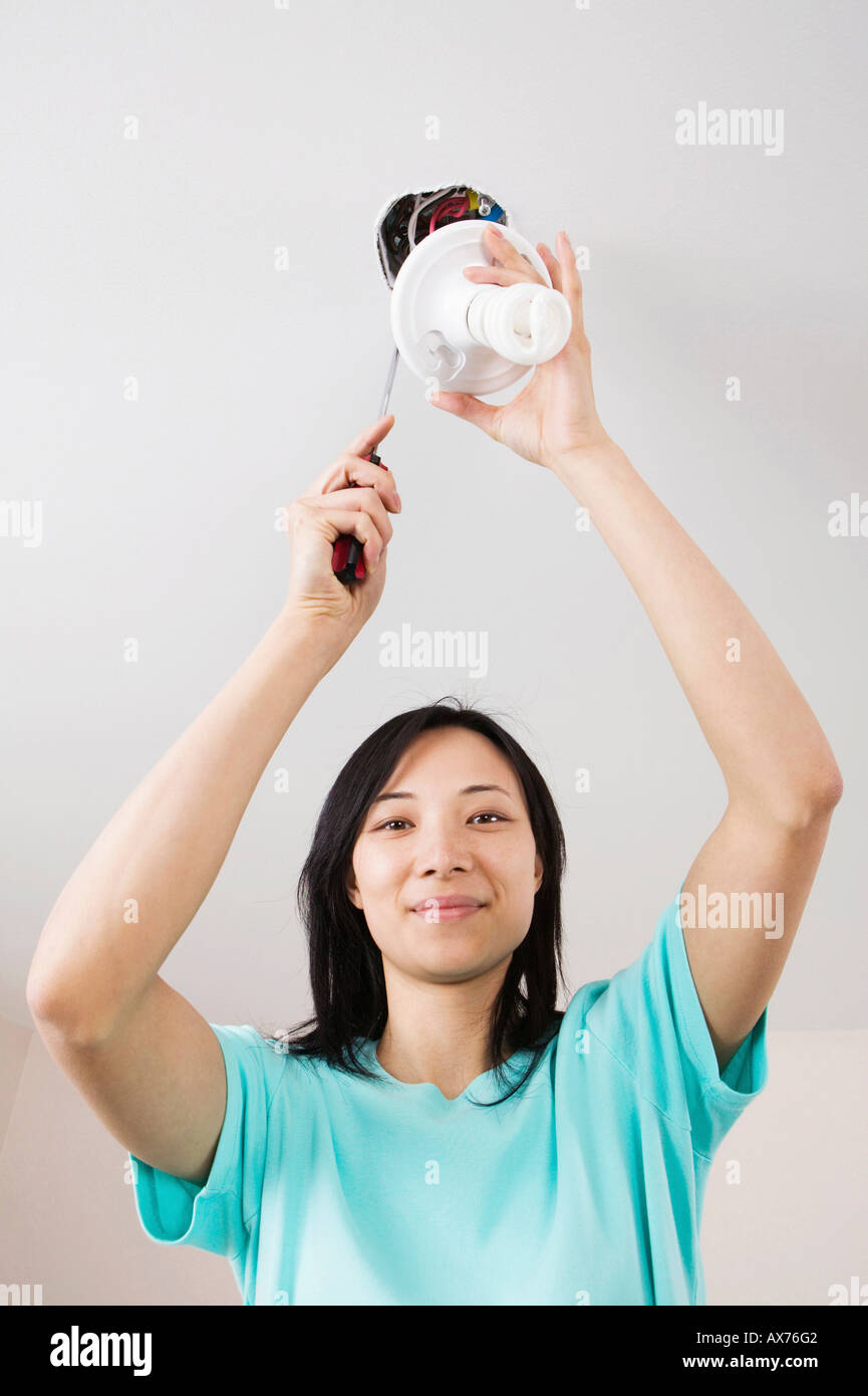 Low angle view of a young woman fixing a light fixture Stock Photo