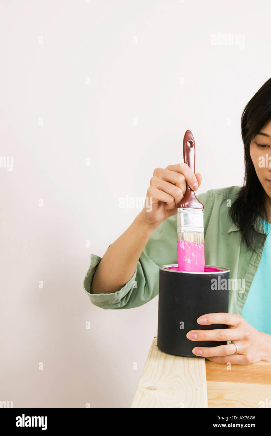Close-up of a young woman dipping a paintbrush into a paint can Stock Photo