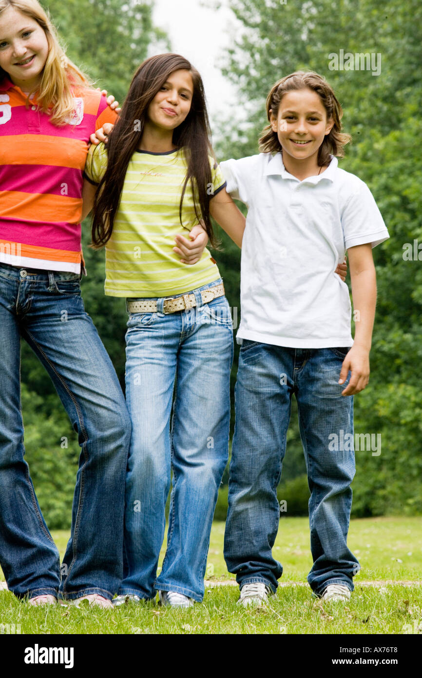 Portrait of two girls and a boy standing in a park with their arms ...