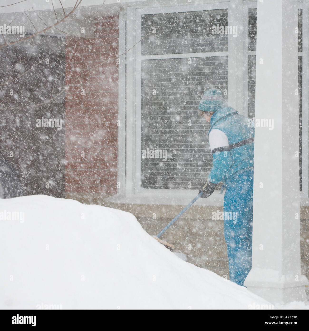 Clearing Snow A woman in a blue snow suit brushes snow off a porch while large fresh flakes pour down Stock Photo