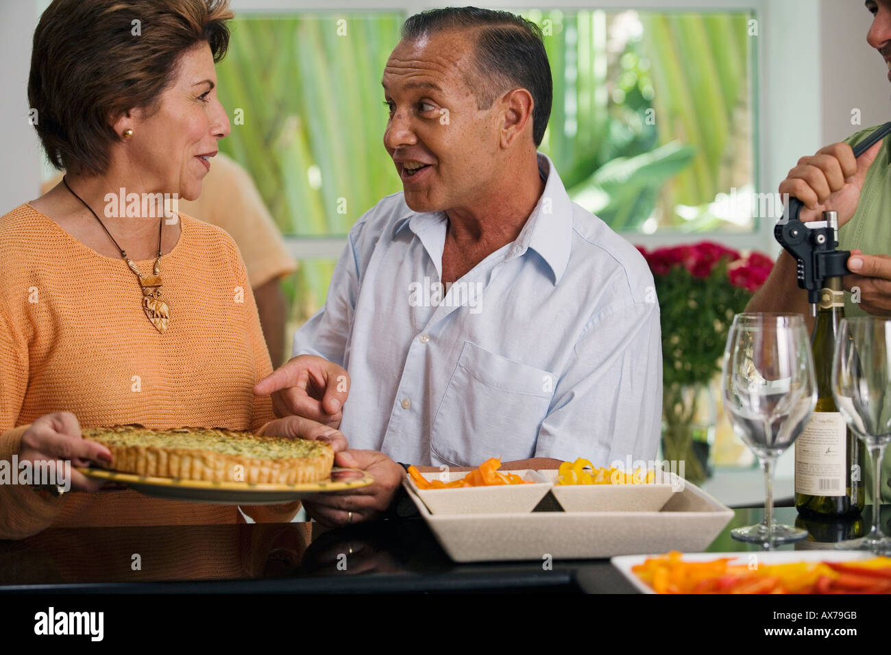 Close-up of a mature couple talking to each other with a mature man unscrewing the cork of a wine bottle Stock Photo