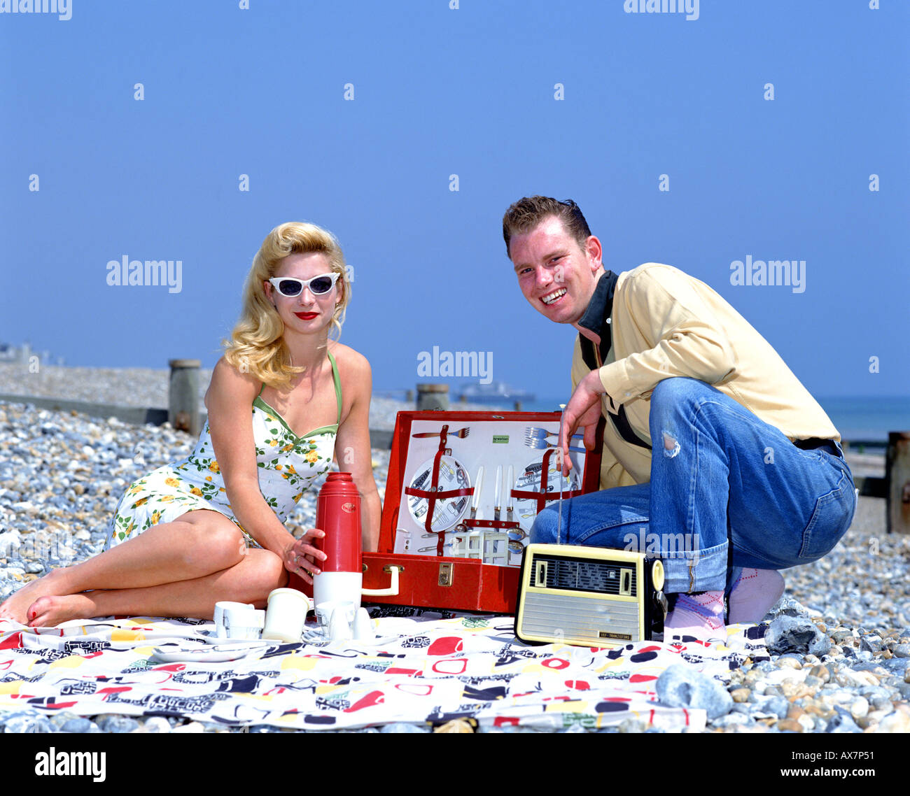 50s Style Couple sitting on the beach with picnic hamper Stock Photo