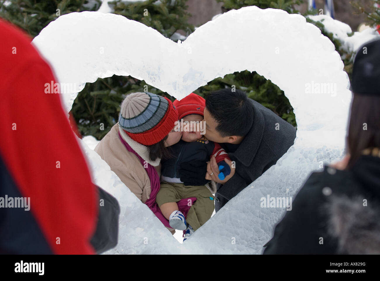 An oriental family kissing their son framed by heat ice sculpture during annual Winterlude activities in Ottawa Canada Stock Photo