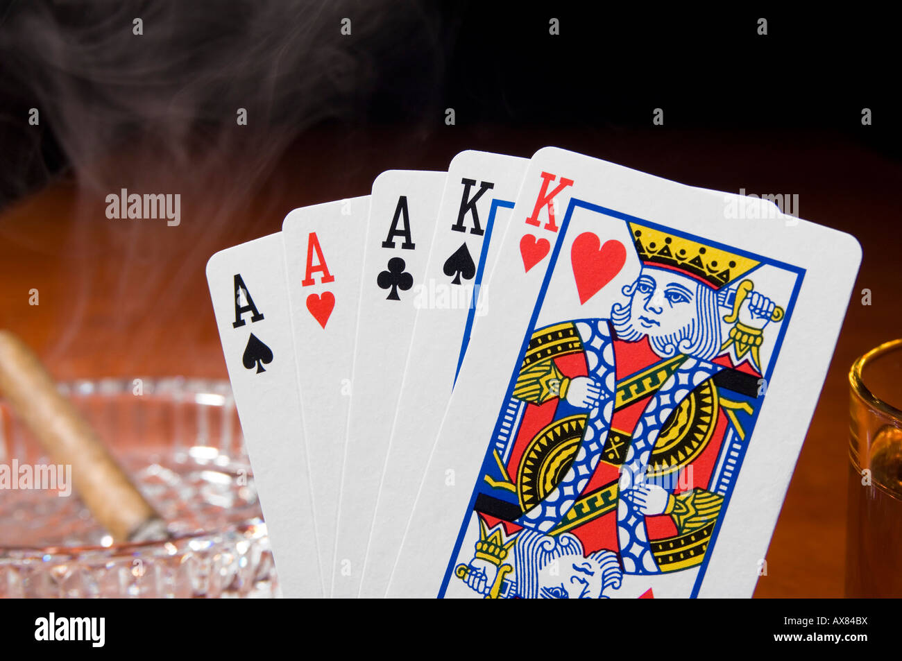 A hand of poker showing aces-high full house with a smoking cigar on the table Stock Photo