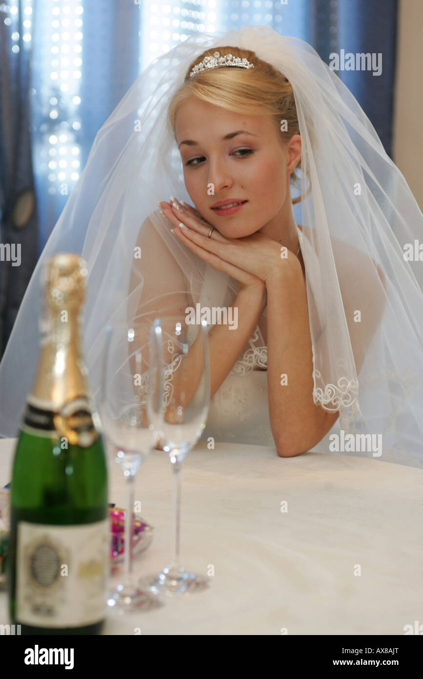 Thoughtful bride wearing veil with champagne bottle in foreground Stock Photo