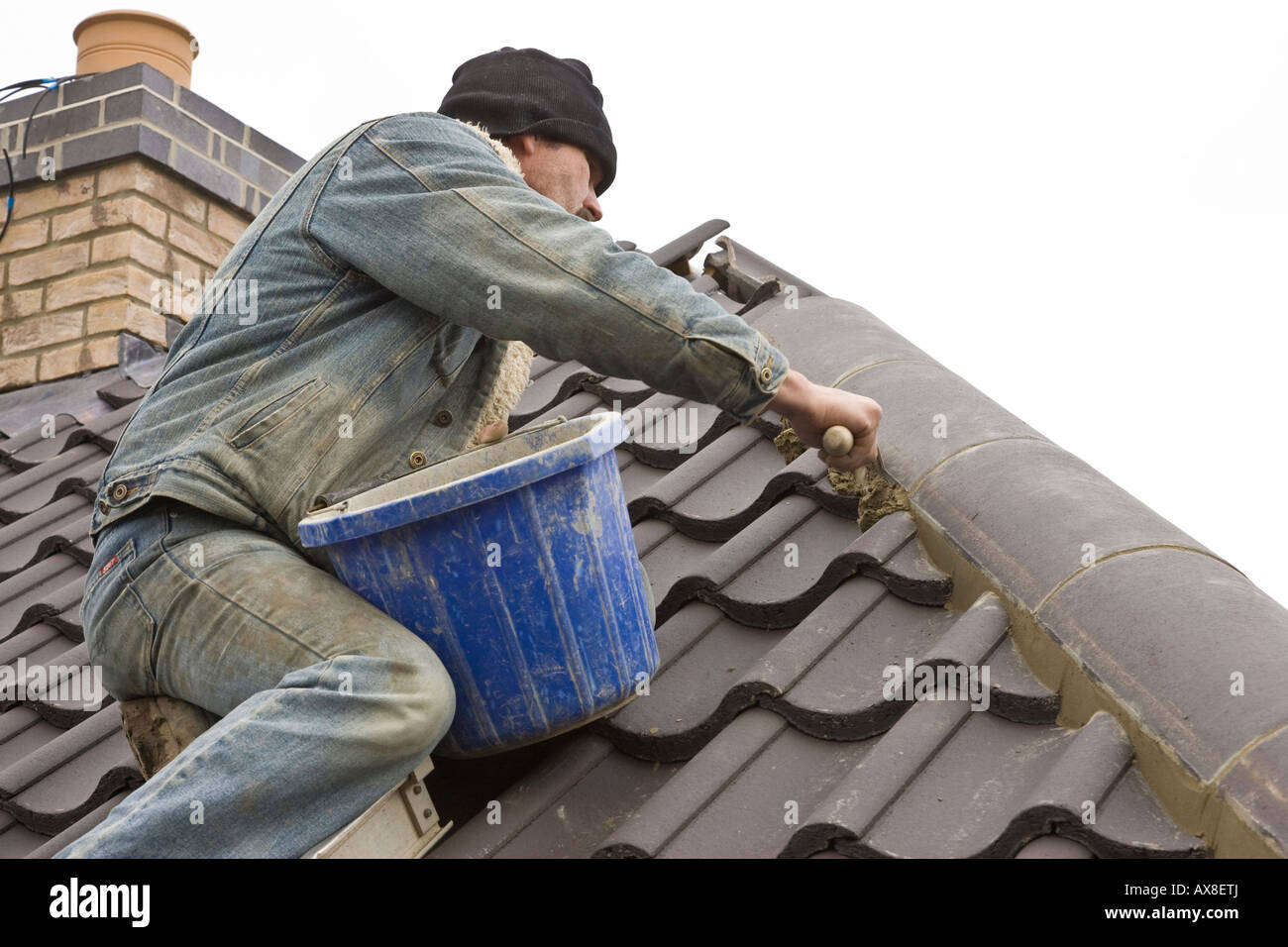 builders smoothing mortar and fitting ridge tiles to a roof of a new