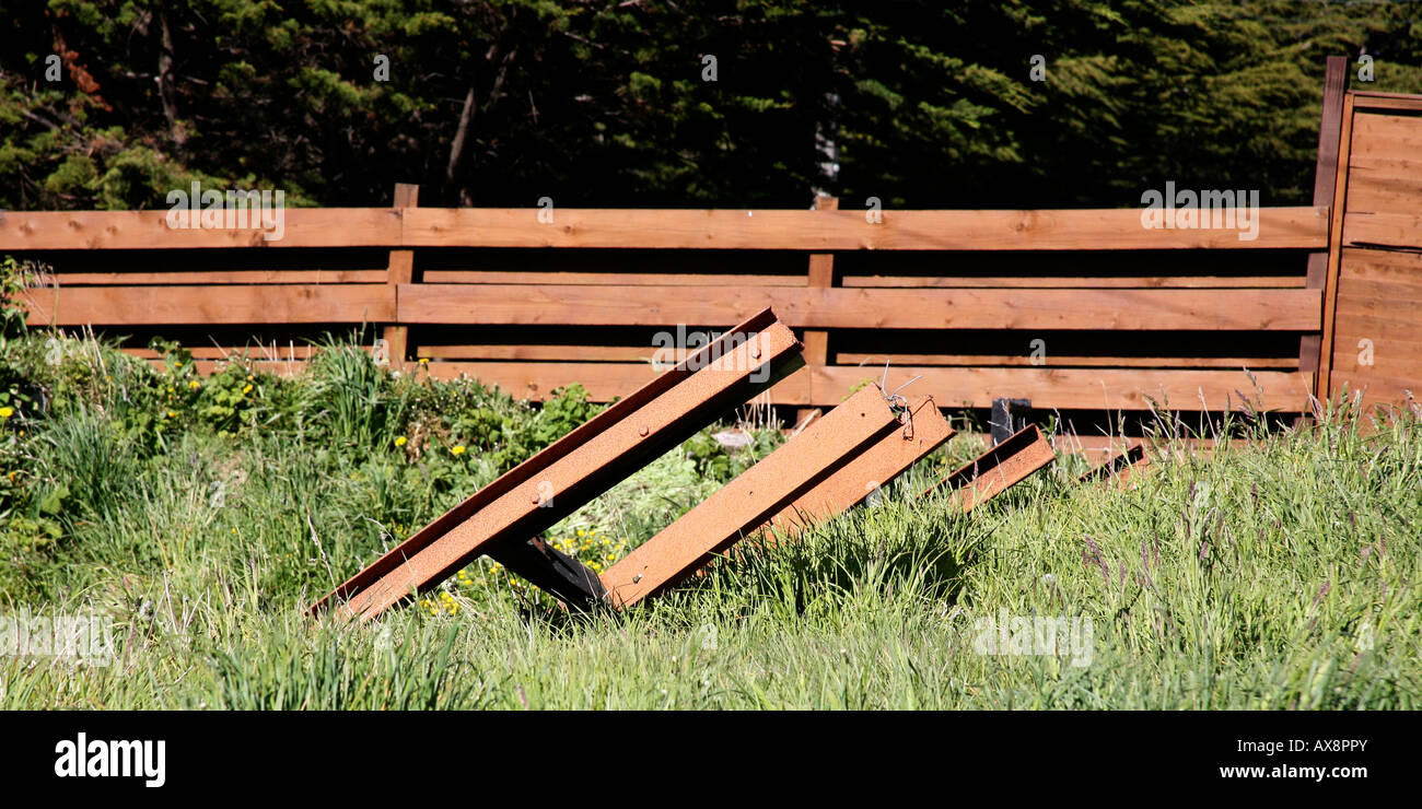 metal rails or girders in overgrown yard with wood fence of same color in background Stock Photo