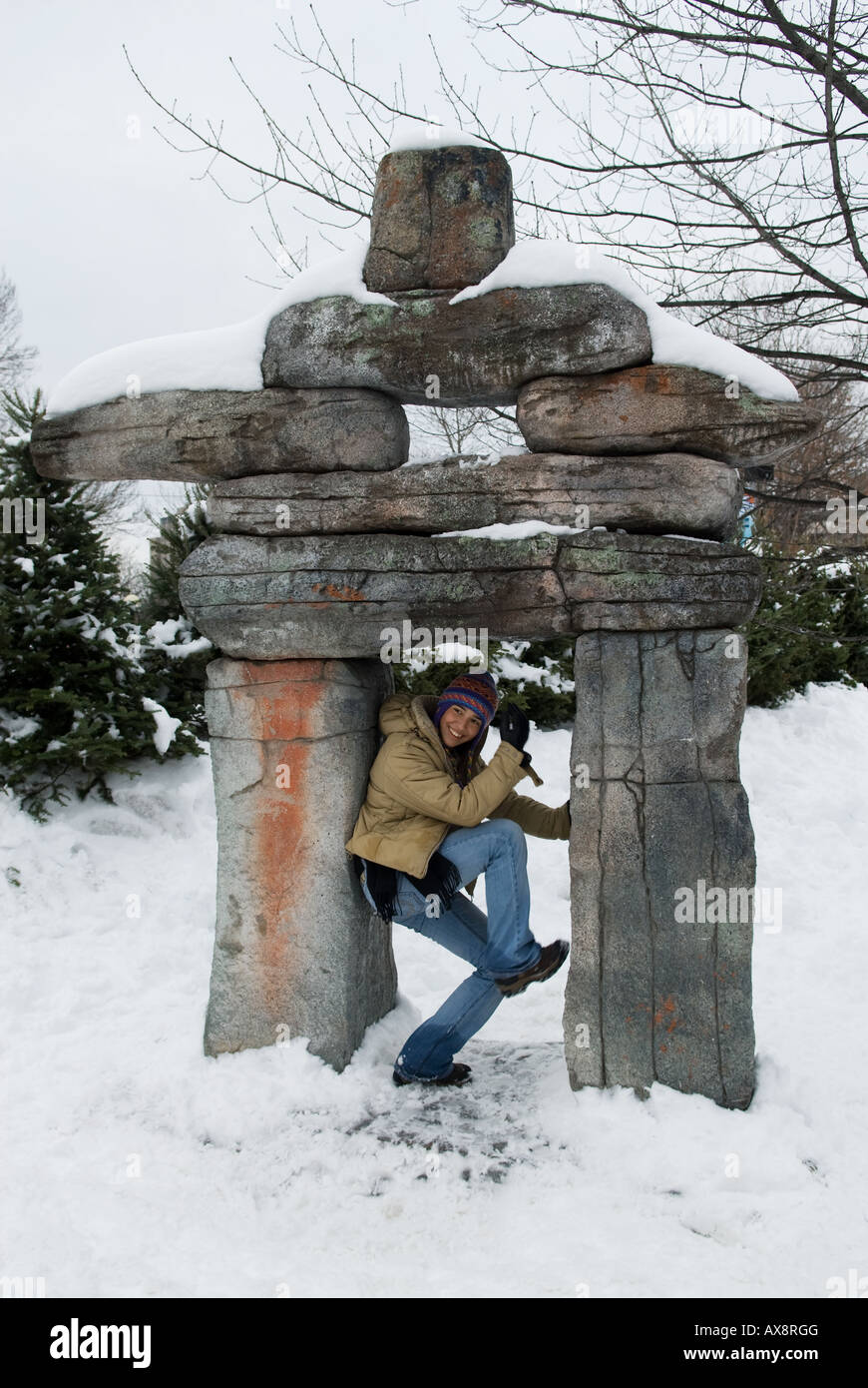 A native poses between the legs of an Inuskshuk Inuit art sculpture during annual Winterlude activities in Ottawa Canada Stock Photo