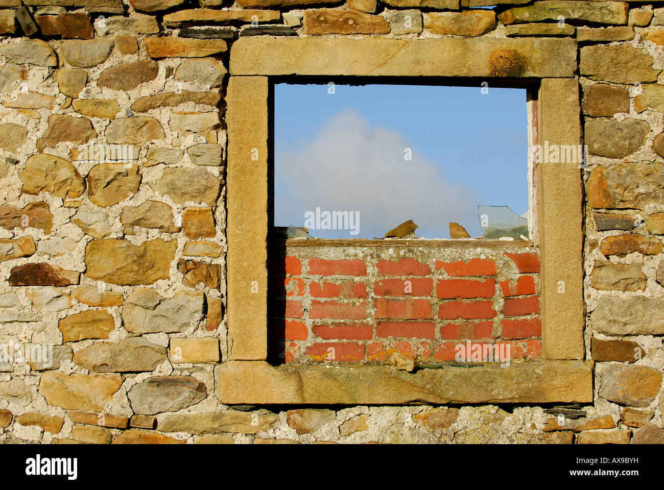A stone wall with a window frame shows the sky, with broken glass and ...