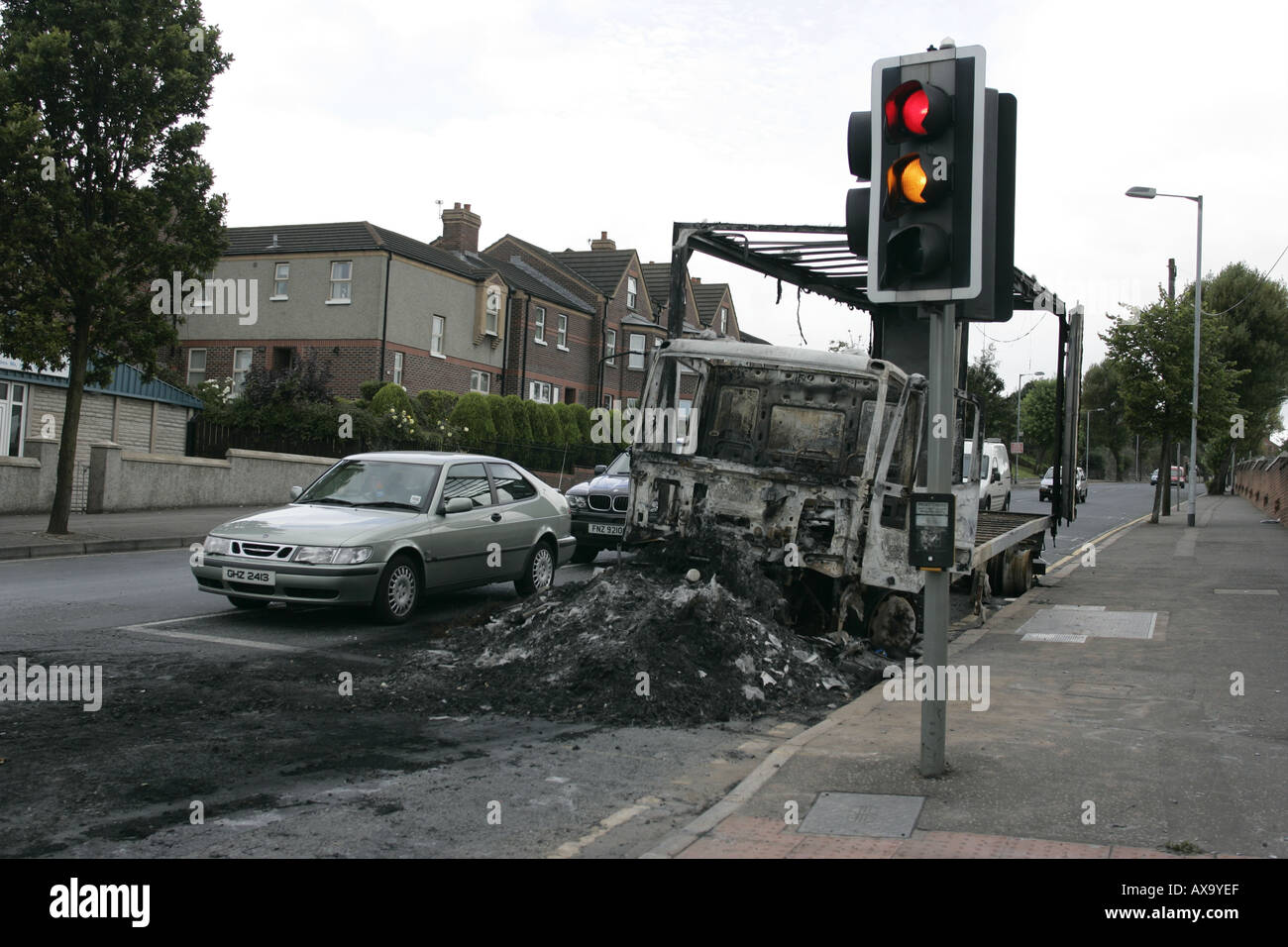 car passes remains of burnt out lorry van at traffic lights after