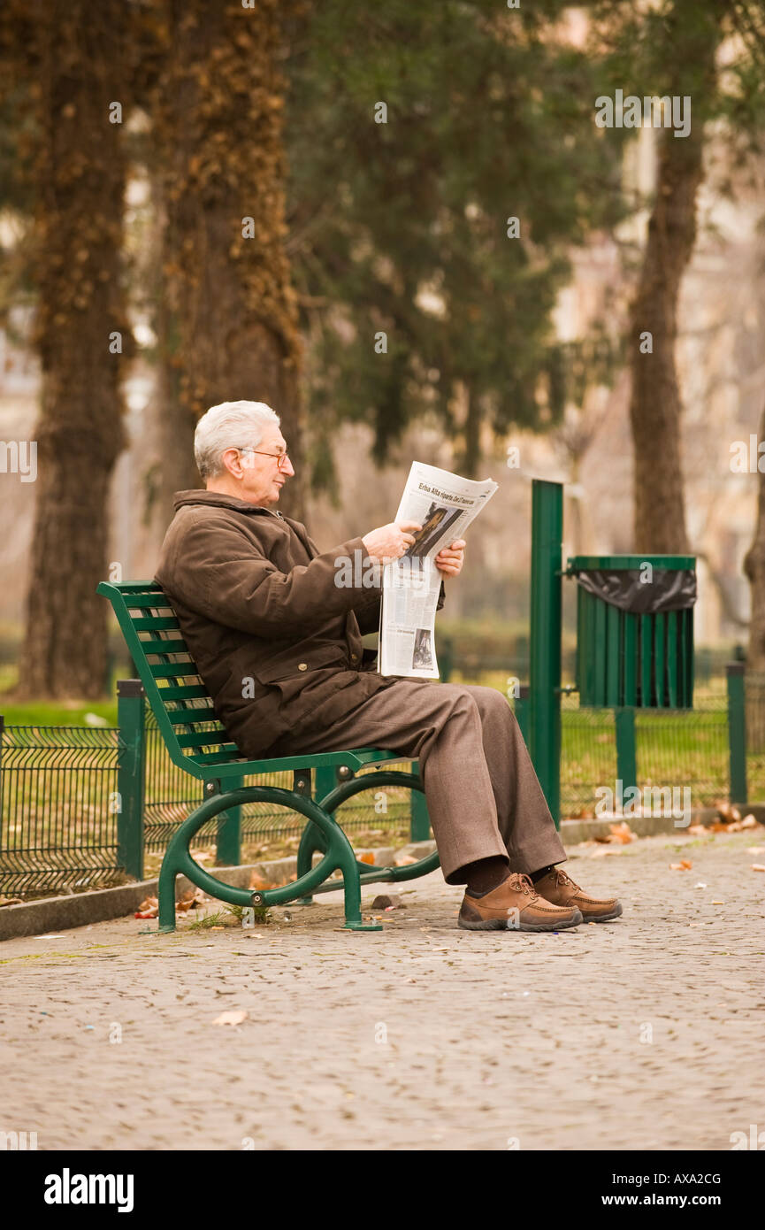 AN OLD ITALIAN MAN READING A NEWSPAPER ON PARK BENCH COMO ITALY Stock Photo