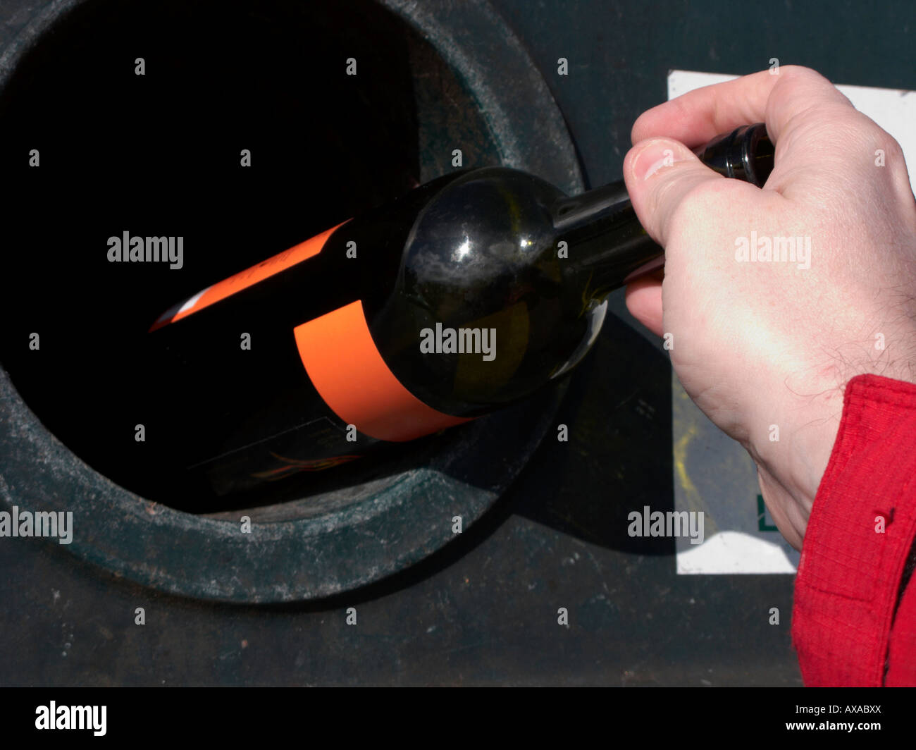 mans hand placing a empty green wine bottle in a recycling bottle bank