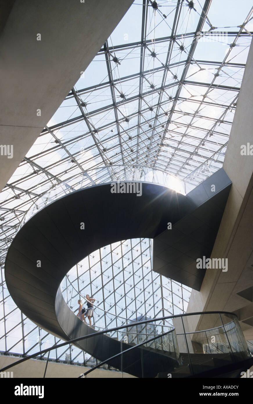 Patrons walk up interior stairs of Glass Pyramid in Louvre Paris France Stock Photo