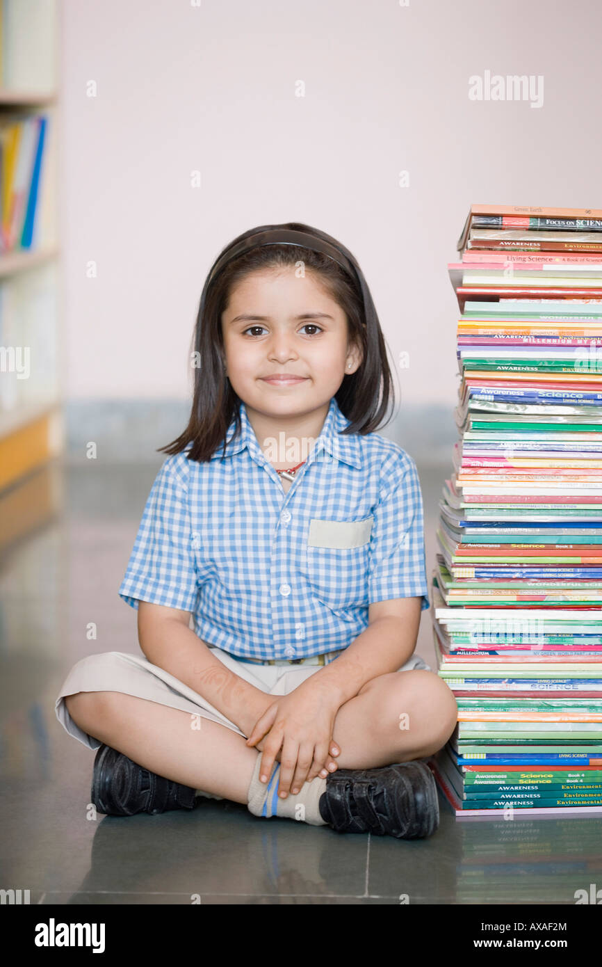 Portrait of a schoolgirl sitting on the floor with a stack of books ...