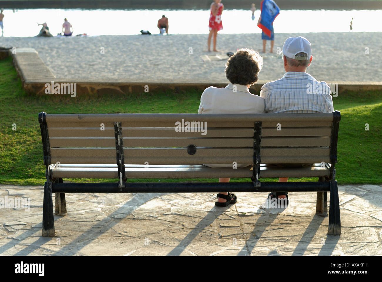 Retired couple sitting on a park bench at the end of the day on Waikiki Beach O'ahu Hawaii Stock Photo
