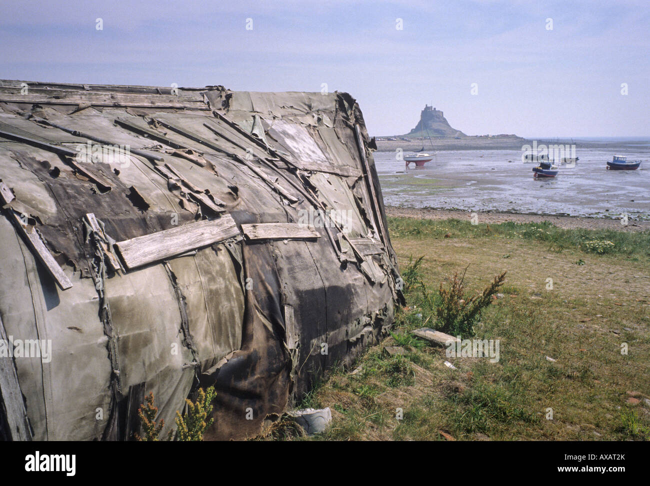 Shed made from upturned boat, Holy Island, Lindisfarne, Northumberland. Lindisfarne Castle in the distance across the bay Stock Photo