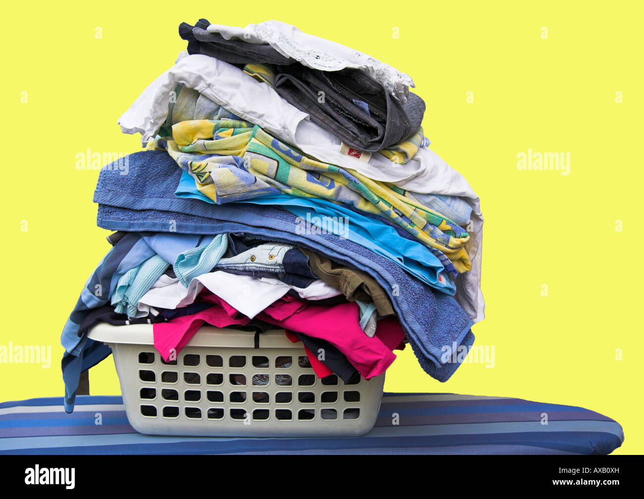 Washing basket full of clothing, with a yellow background. Stock Photo