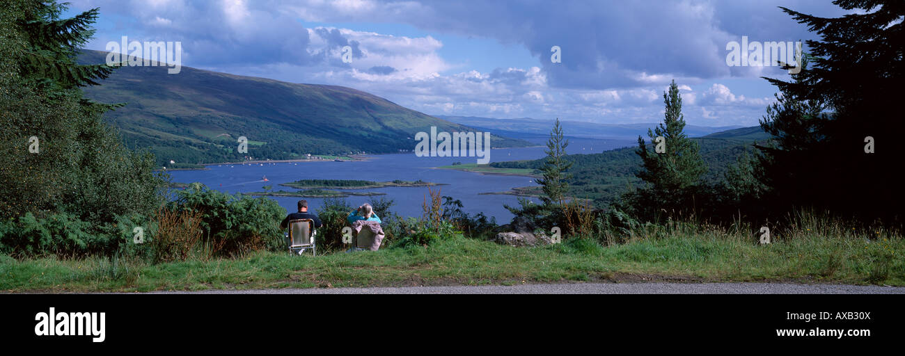 Panoramic summer scene of two people seated looking down over the beautiful sea and hills of the