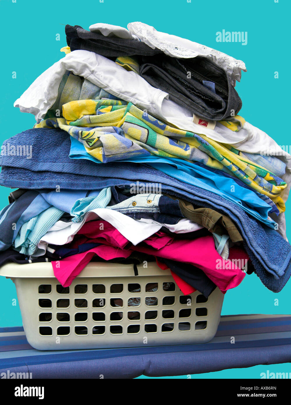Washing basket full of clothing, with a blue background. Stock Photo