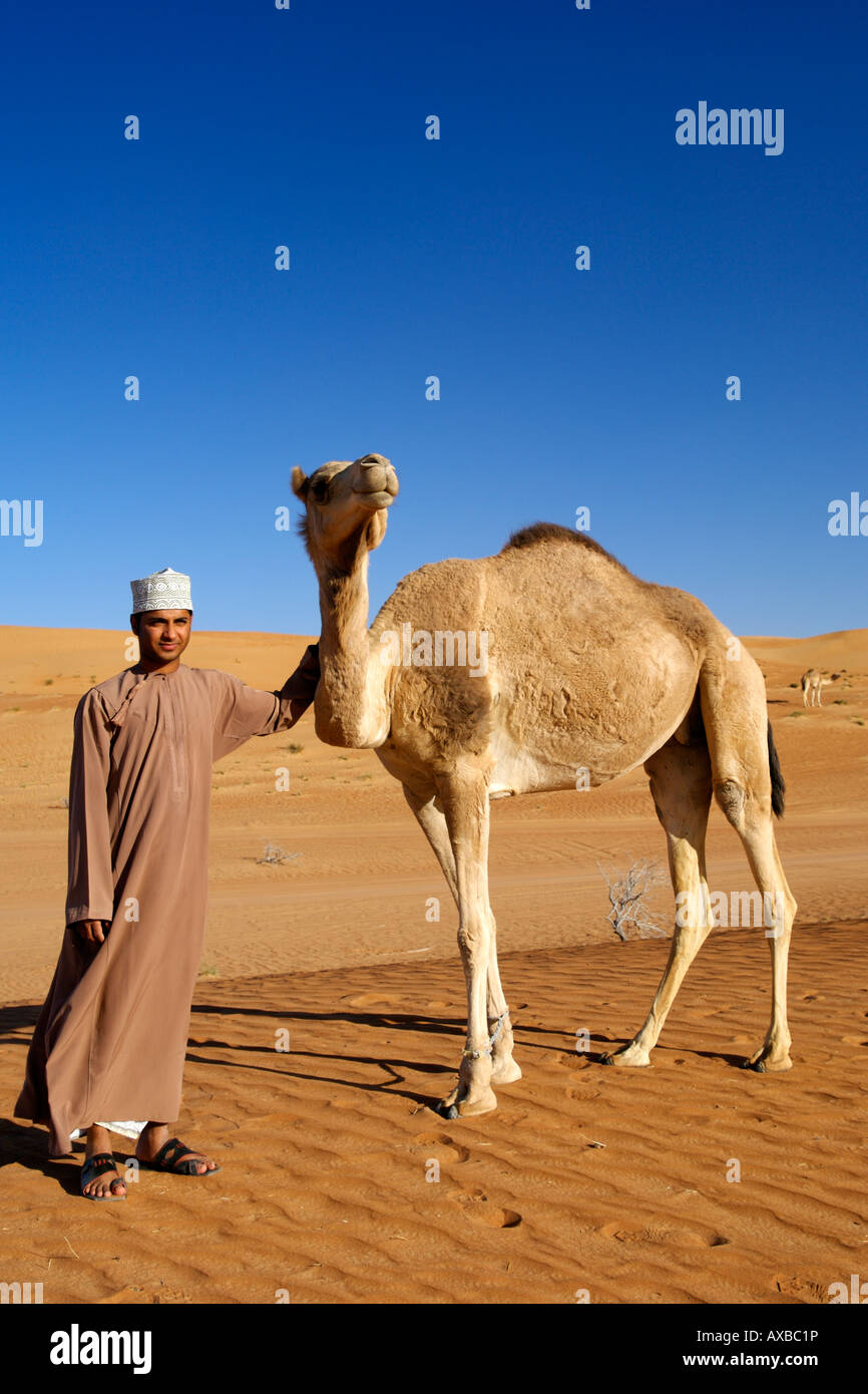 An Omani man standing with an Arabian camel a.k.a. a one-humped dromedary (Camelus dromedarius) in Wahiba Sands in Oman. Stock Photo