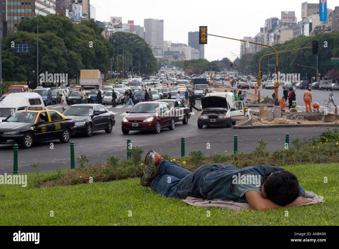 Homeless man sleeping on a grass verge in the middle of Avenida 9 de Julio (A) Stock Photo
