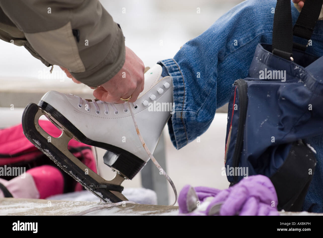 A young girl looks on as her father helps tie on ice skate during Kingstons annual FebFest winter activities Stock Photo