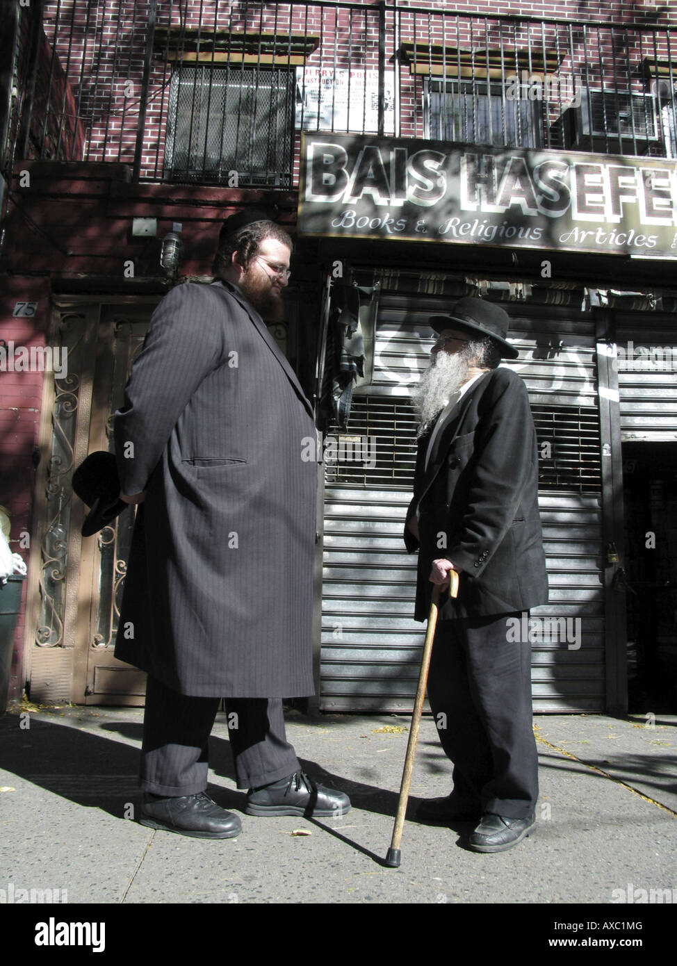 A very tall and a little jewish man in traditional clothes chatting on the sidewalk, USA, Brooklyn, New York Stock Photo