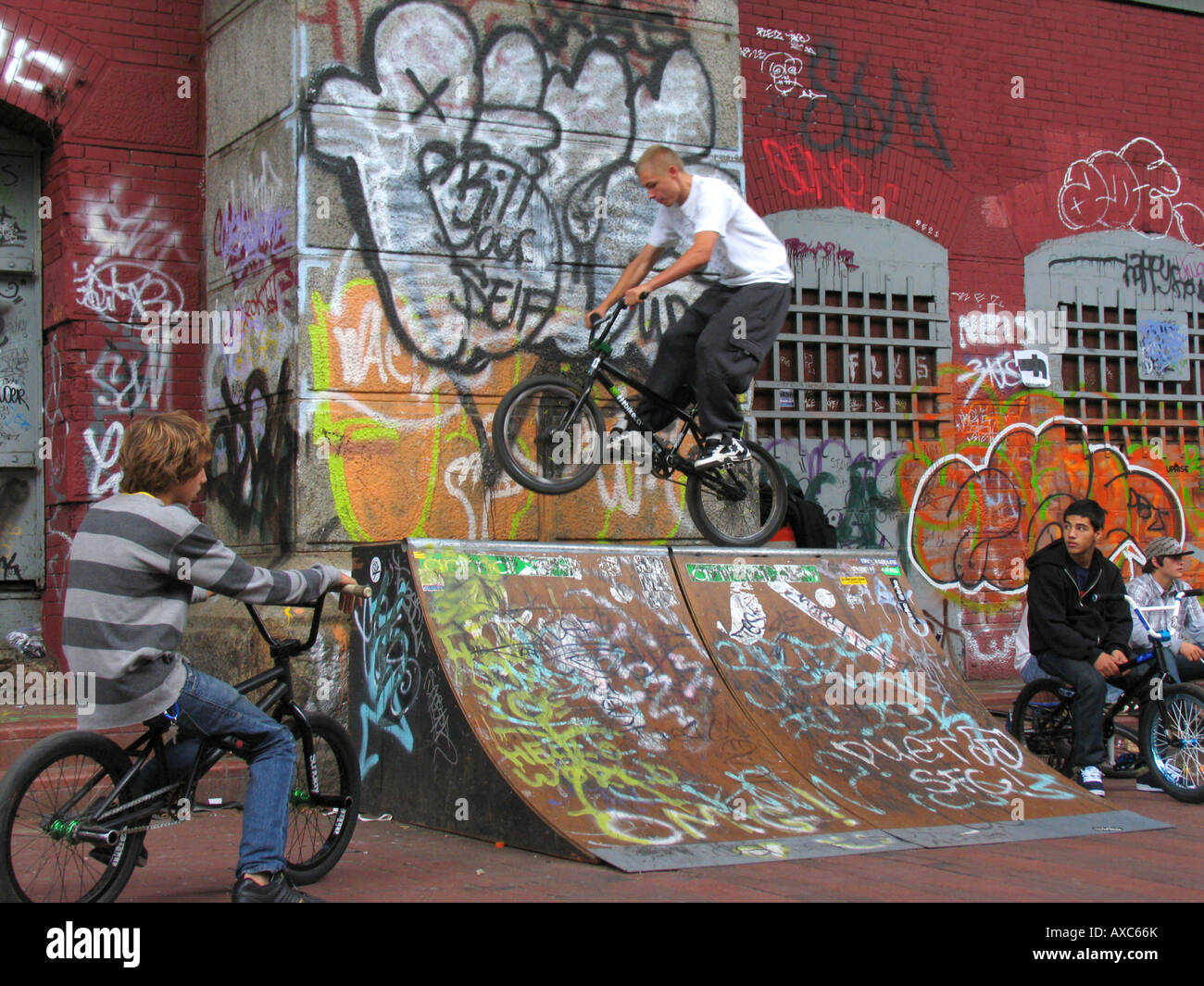 young persons riding BMXbikes on ramp in front of wall with graffiti under the ManhattanBridge