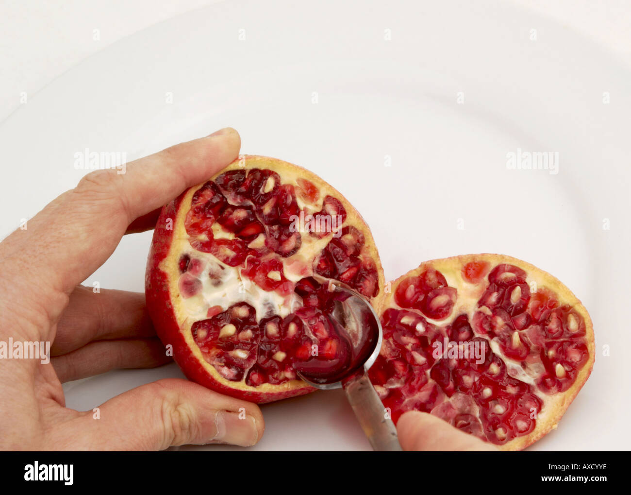 man eating seeds from a sliced pomegranate on a white plate Stock Photo