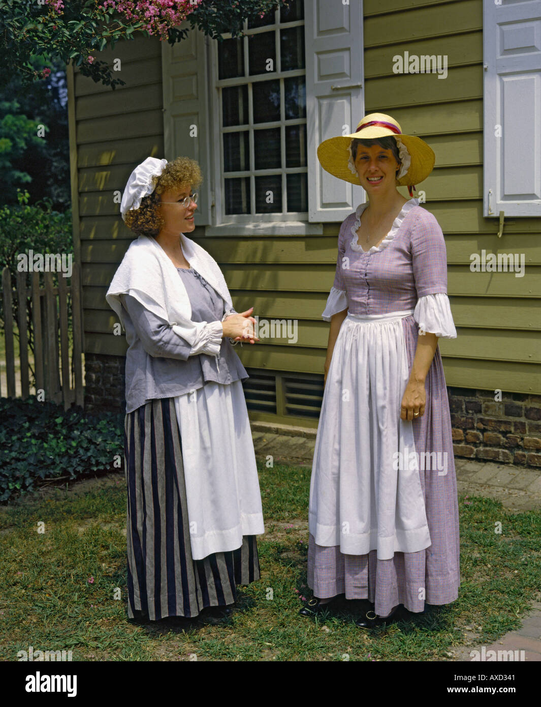 Two ladies in traditional costume in front of clapboard Georgian house in historic Colonial town of Williamsburg Virginia USA Stock Photo