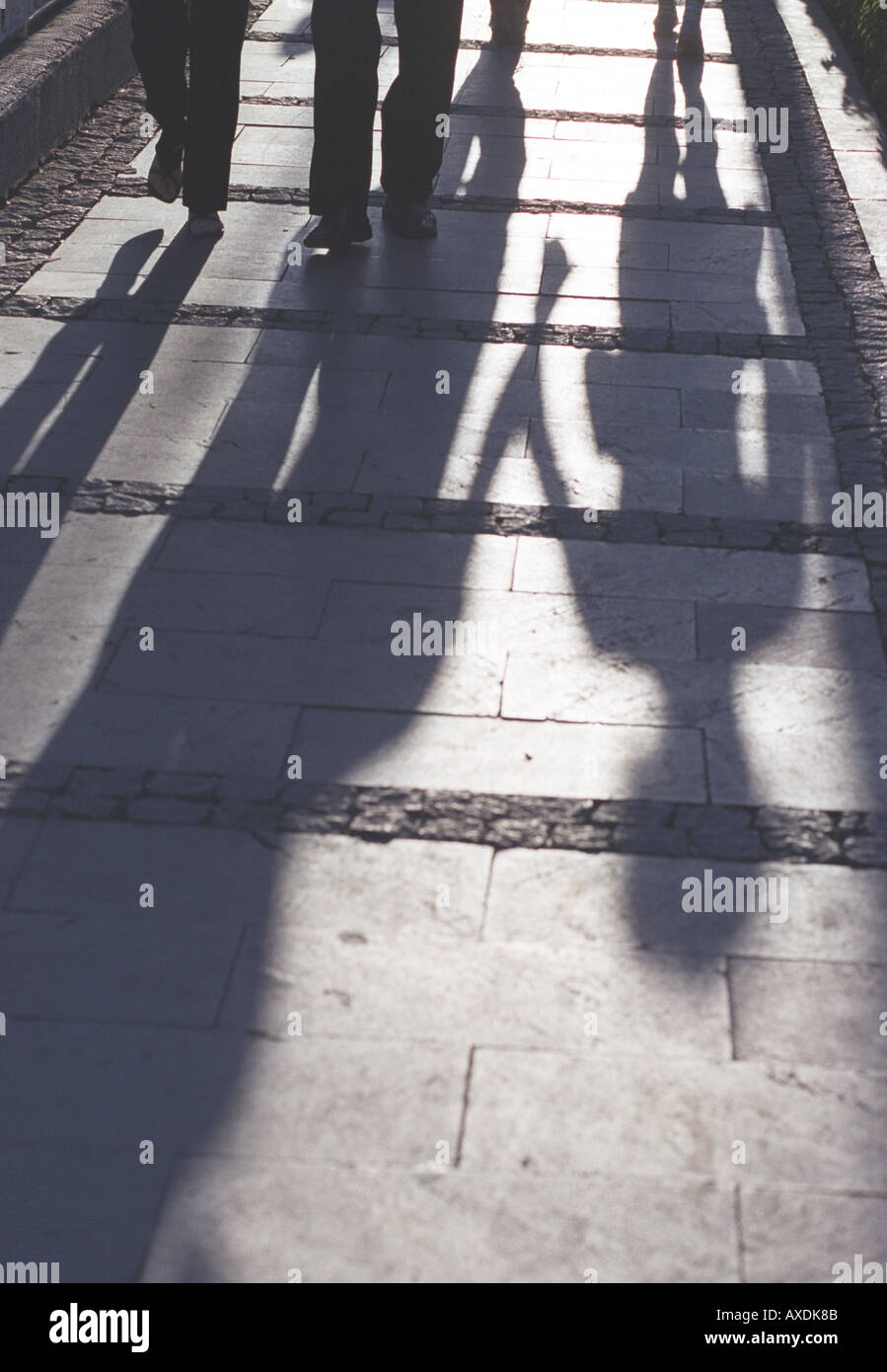 shadows of pedestrians vertical color architecture detail sidewalk brick walkway people pedestrians legs walking movement shadow Stock Photo