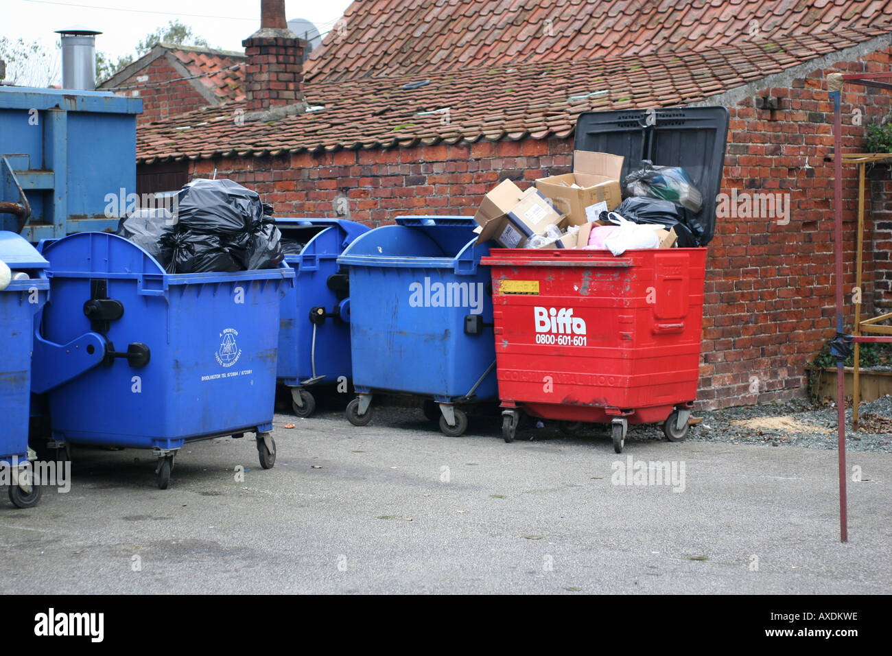 Series of coloured waste skips or dumpsters largely full to overflowing ...