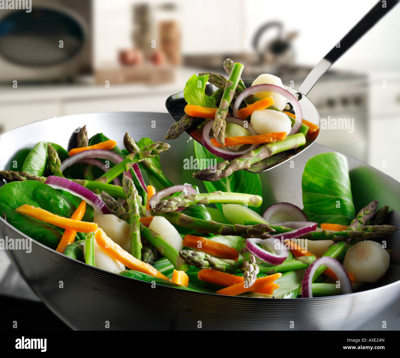 Vegetable stir fry in a wok being stirred with asparagus, red onions, bean shoots, pak choi and vegetables Stock Photo