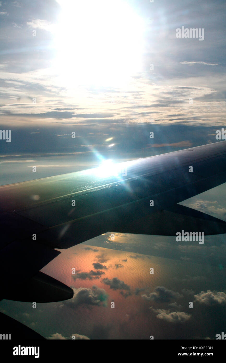 overhead aerial bird's-eye-view of sunlight reflecting off aircraft wing flying over a lake lit up with a golden glow Stock Photo