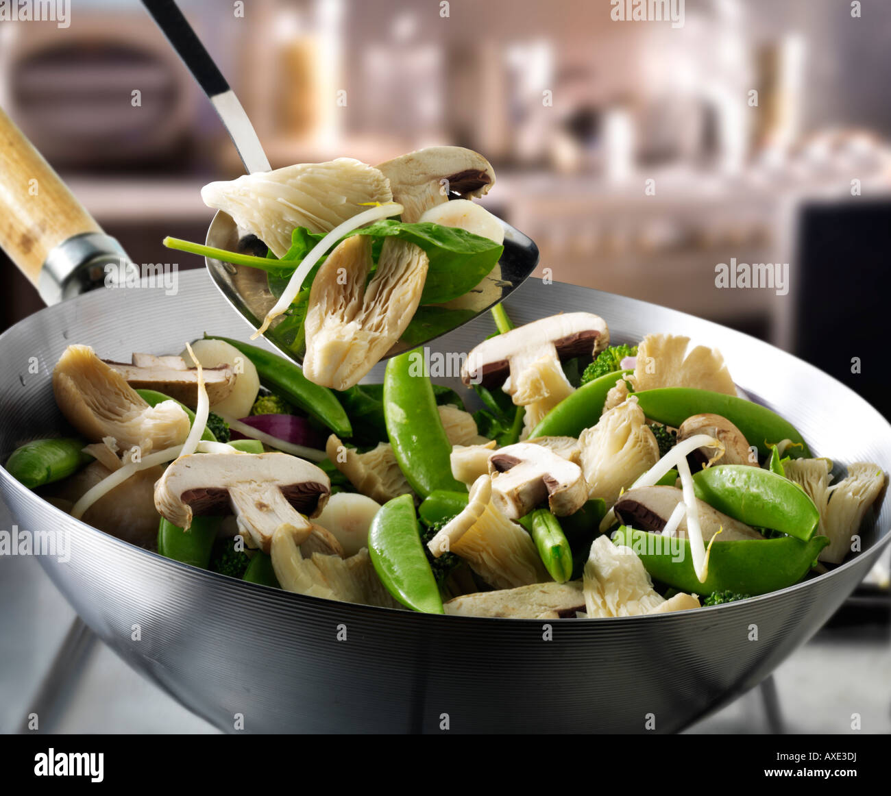 Vegetable stir fry in a wok being stirred with Shataki and oyster mushrooms, mange tout and vegetables Stock Photo