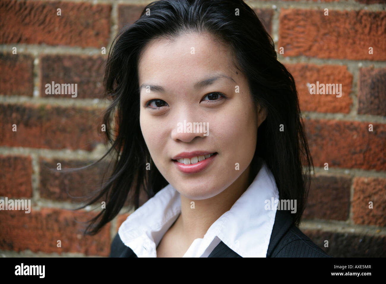 Portrait of a Young Chinese Woman in a Business Suit in Front of a Brick Wall Stock Photo