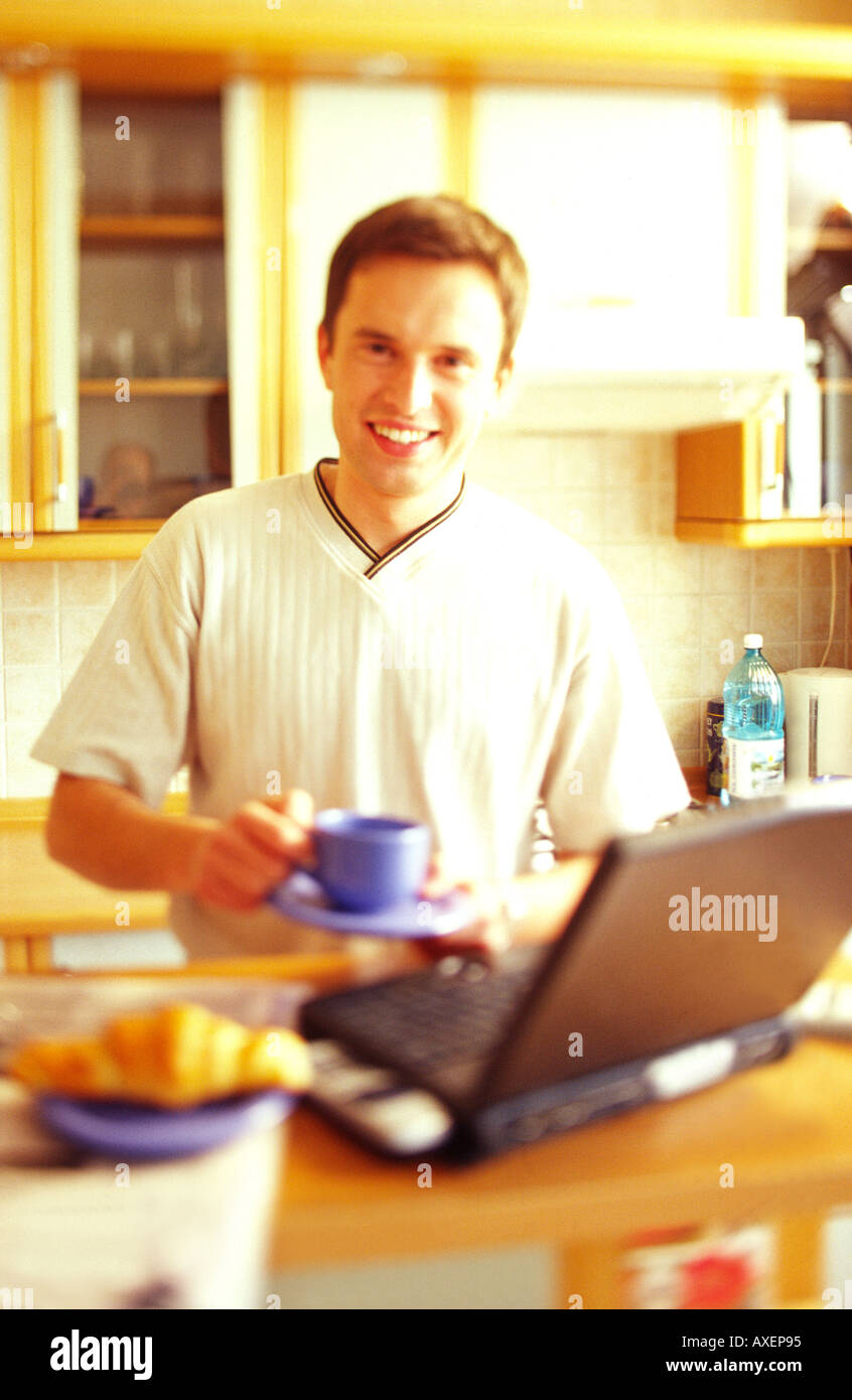Young man drinking from a cup while using a computer. Stock Photo