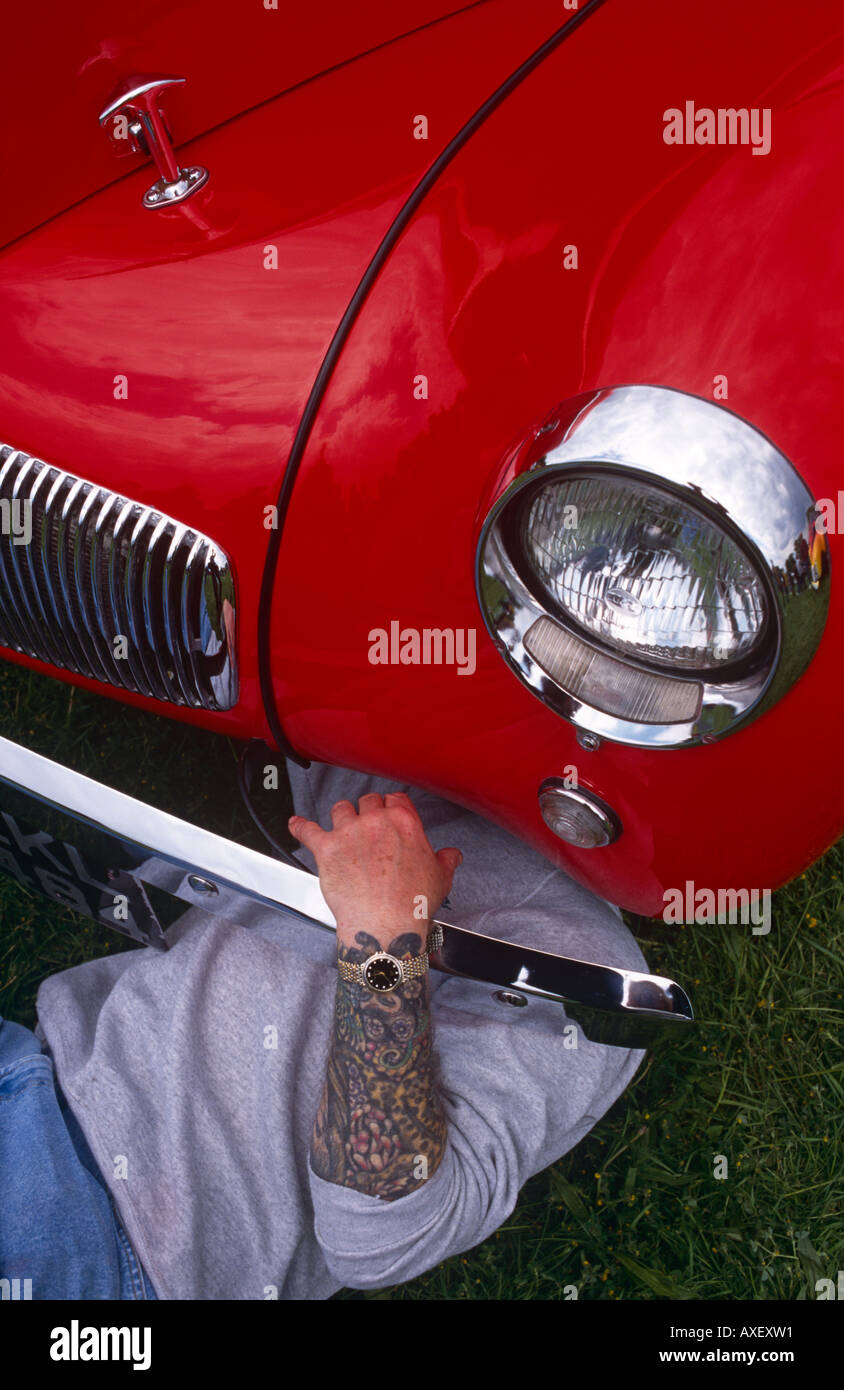 A classic car hobbyist sporting a tattoo on his arm, examines the underside of his red Ford Anglia at a car rally, UK Stock Photo - Alamy
