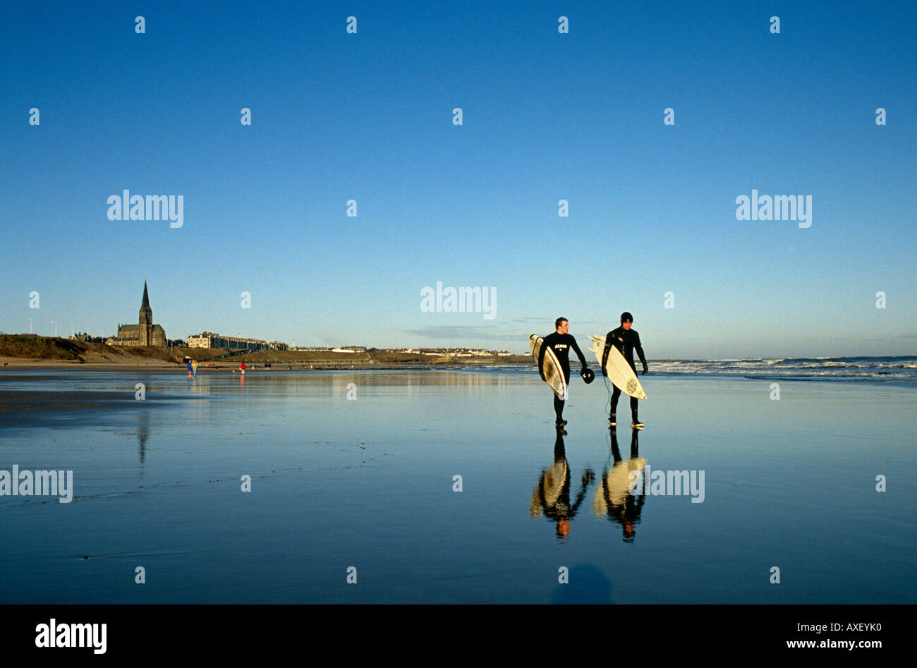Two surfers carry their boards out to the surf on the beach at Cullercoats, Tyneside, England UK. Stock Photo